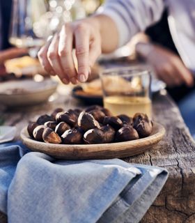 Una persona allunga la mano per prendere delle caldarroste da un piatto di legno
